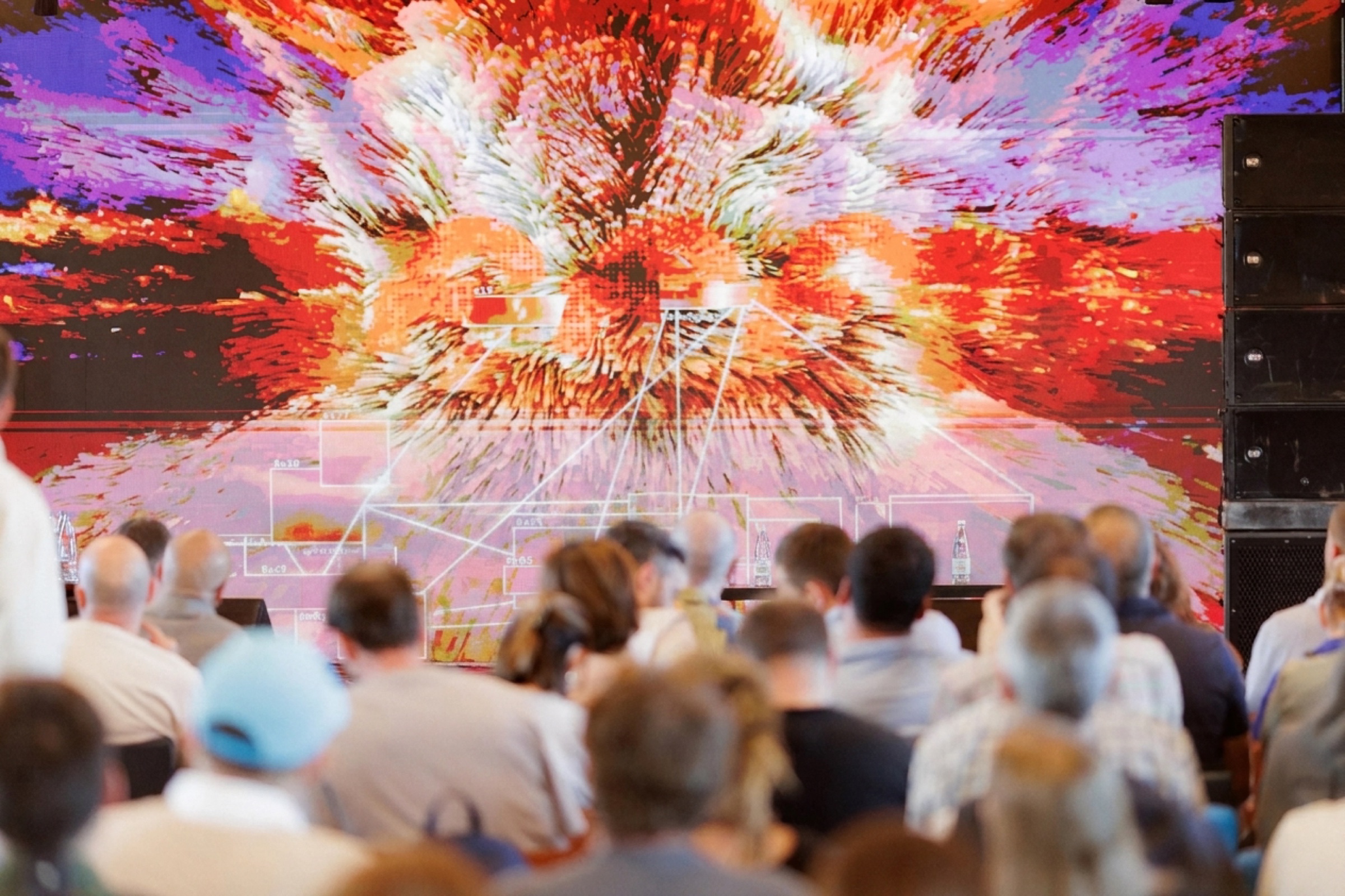 Audience facing a large LED wall showing AI-generated particle footage of an exploding landscape in red and orange